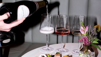 Champagner wird in ein Glas gegossen, das auf einem Tisch steht, daneben kleine Häppchen.