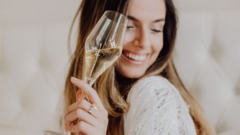 Lächelnde Frau mit einem Glas Sekt in der Hand in hellem Ambiente im Restaurant Veranda.