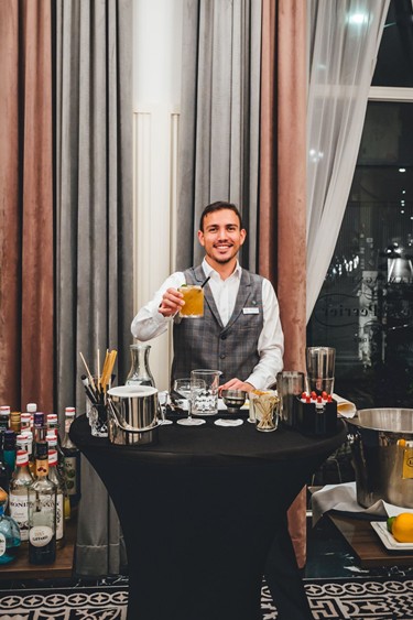 Become a cocktail pro A bartender proudly presents a cocktail while standing at a cocktail bar.