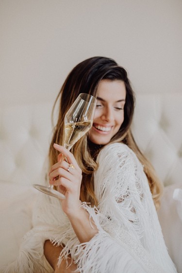 Lächelnde Frau mit einem Glas Sekt in der Hand in hellem Ambiente im Restaurant Veranda.