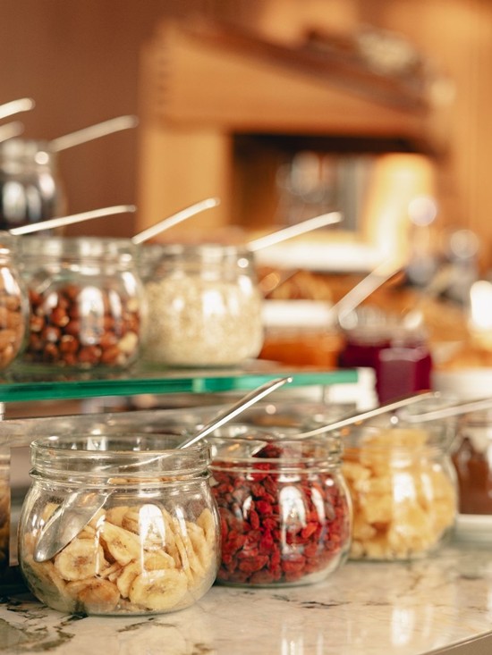 Ein Buffet mit einer großen Auswahl an verschiedenen Müsli-Zutaten, Nüssen und Trockenfrüchten für ein gesundes Frühstück.