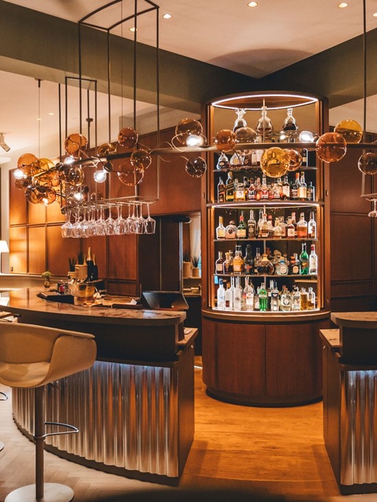 Blick auf die Bar im Restaurant Veranda mit eleganter Beleuchtung und einer Auswahl an Spirituosen.