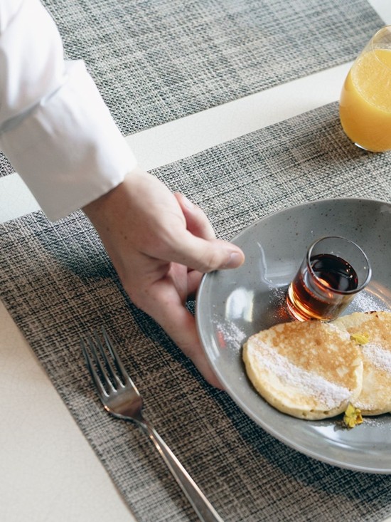 Service trainee during a summer internship serving freshly prepared pancakes to a young guest at Restaurant Veranda.
