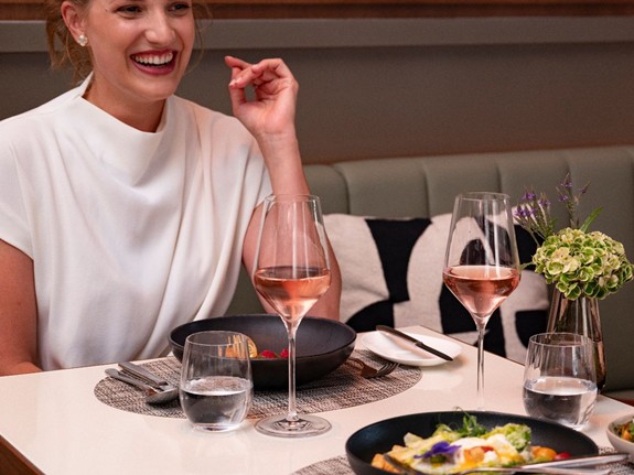 Perfektes Dinner für unvergessliche Momente Eine Frau genießt ein leckeres Dinner mit einem Glas Rosé und einer Schüssel frischem Salat.